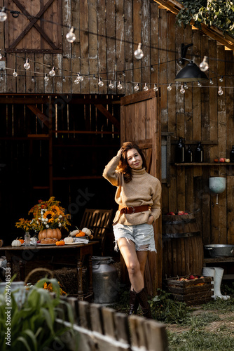 Beautiful cozy fall farm house interior. Portrait of pretty woman in a warm sweater. Handmade table decor with pumpkins, sunflowers, countryside style. Sunset, cosy atmosphere, autumn colours