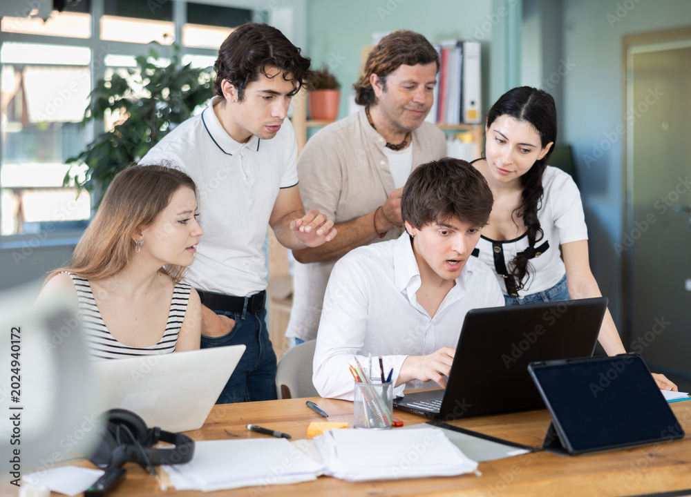 Fototapeta premium Team of employees gathers around single laptop, looking at screen and collaborating on common project or problem