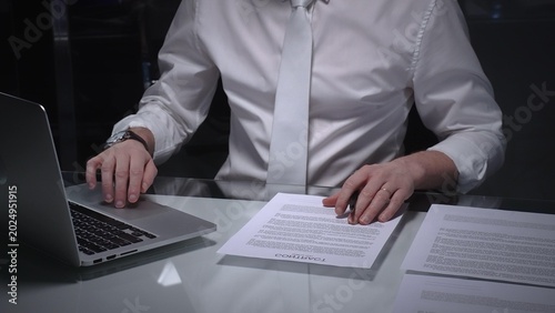 Photos Businessman in white shirt reviewing legal documents, checking details of a contract with a magnifying glass on a dimly lit desk