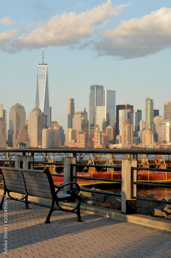 Obraz premium Illuminated Seat Along Waterfront Enjoying Peaceful Cityscape And Gentle Shadow Play new york