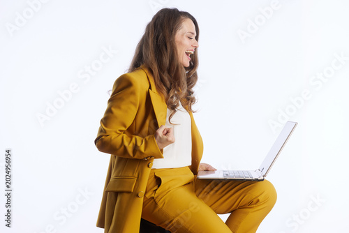 Foto A triumphant businesswoman in a yellow pantsuit celebrates a significant achievement while looking at her laptop, radiating success and excitement in her work
