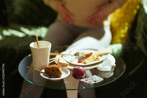 A person clutches their stomach in discomfort near a table littered with unhealthy food remains and medication, symbolizing the consequences of a poor diet.