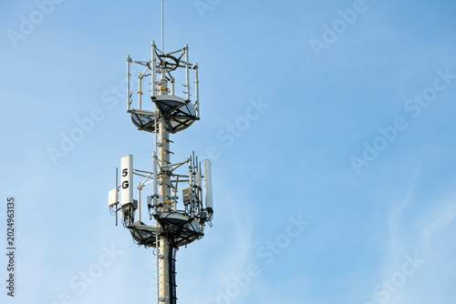 Сlose-up shot of a telecommunications tower equipped with modern 5G cellular antennas and transmitters against a clear blue sky. High-tech wireless communication network infrastructure.