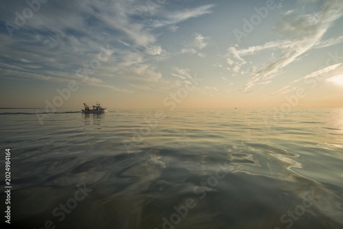 Golden sunset over the calm Tyrrhenian Sea near Viareggio, Italy, with a small fishing boat silhouetted against the warm glowing horizon.