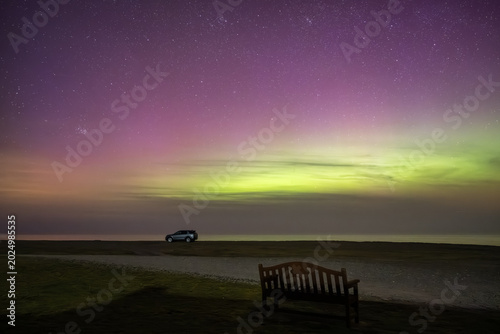 Traveling and van life concept. Campervans and motorhomes parked at Point of Ayre, Isle of Man, under a spectacular night sky illuminated by the vibrant green and purple bands of the Northern Lights.