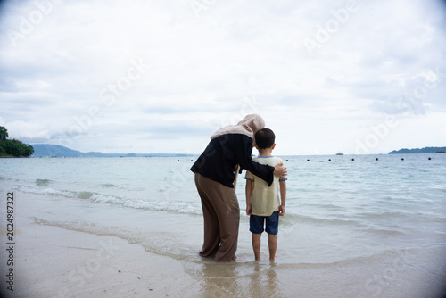 Portrait of a mother and son standing on the beach looking at the calm sea while chatting with their child, a calm and comfortable atmosphere during the holidays.