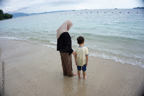 Portrait of a mother and son standing on the beach looking at the calm sea while chatting with their child, a calm and comfortable atmosphere during the holidays.