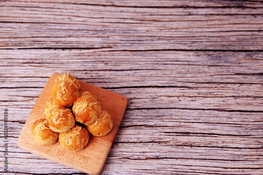 Fototapeta premium Kue Nastar or Golden pastries rest on a wooden board. Warm tones highlight crisp, inviting textures. Rustic wood adds cozy, homey charm. Perfect for food blogs or cafe promotions. 
