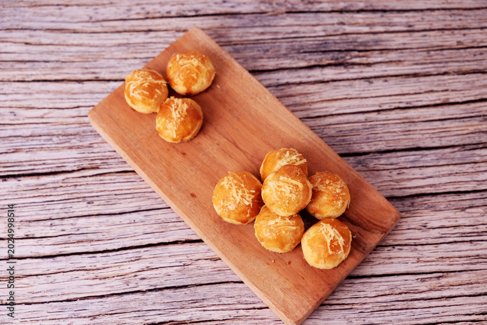 Fototapeta premium Kue Nastar or Golden pastries rest on a wooden board. Warm tones highlight crisp, inviting textures. Rustic wood adds cozy, homey charm. Perfect for food blogs or cafe promotions. 