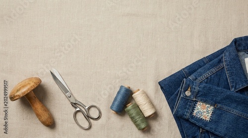 Craft background with sewing accessories and repaired denim jacket on fabric.