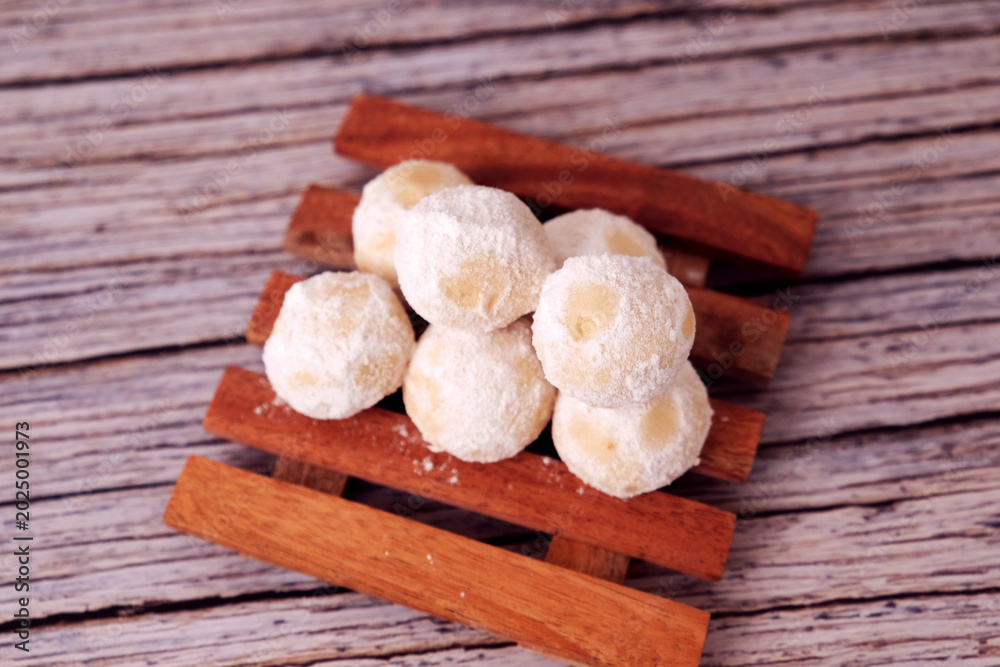Fototapeta premium Kue Salju or Soft, round treats dusted with sugar sit on a wooden board. Wooden planks rest on a rustic tabletop. Shallow depth of field highlights texture and sweetness. Perfect for food blogs