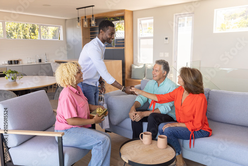Diverse adults standing and exchanging gift bag and potted plant in living room near coffee table