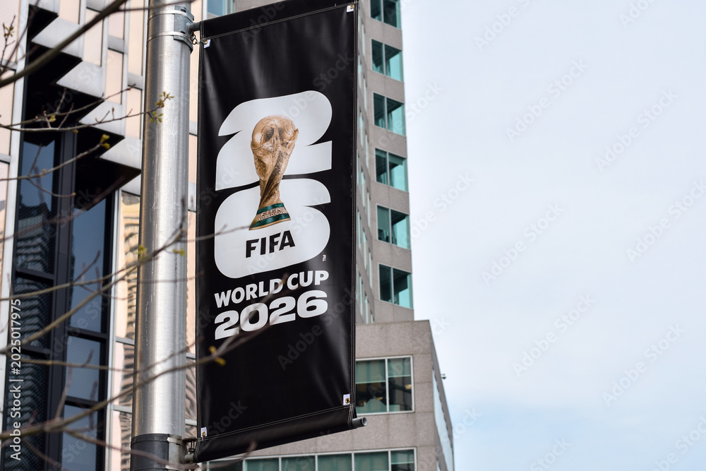 Fototapeta premium Closeup vertical banner promoting FIFA World Cup 2026 attached to street pole in urban downtown Toronto Ontario area with modern office buildings and copy space, May 17 2026