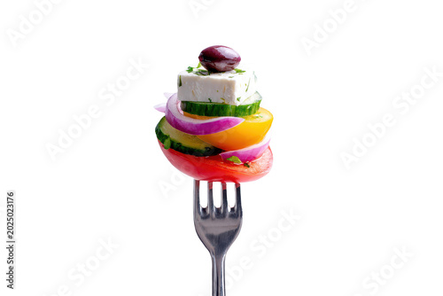 A fork with a skewer of greek salad ingredients including feta cheese, olive, cucumber, tomato, yellow pepper, and red onion isolated on transparent background
