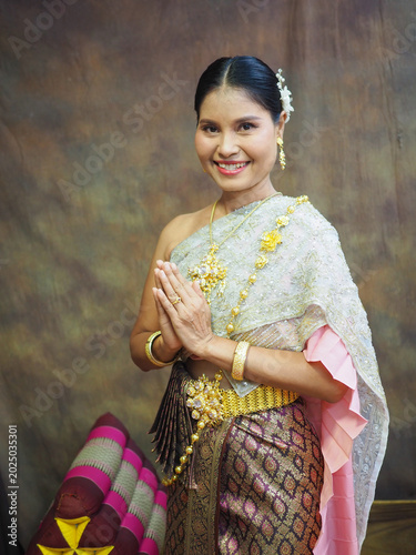 Photography A Thai woman in traditional Thai dress stands smiling and clasping her hands together in a respectful greeting at Wat Chaiwatthanaram in Ayutthaya Province, Thailand