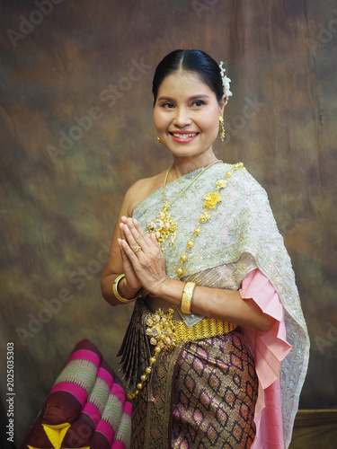 Canvas Print A Thai woman in traditional Thai dress stands smiling and clasping her hands together in a respectful greeting at Wat Chaiwatthanaram in Ayutthaya Province, Thailand
