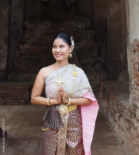 Fotografía A Thai woman in traditional Thai dress stands smiling and clasping her hands together in a respectful greeting at Wat Chaiwatthanaram in Ayutthaya Province, Thailand