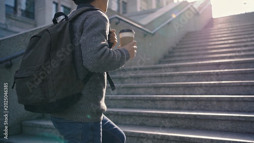 Young Commuter Carrying Backpack and Coffee While Climbing City Stairs at Sunrise