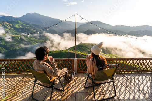 Young couple relaxing and enjoying the sunrise and sipping their morning coffee amidst the beautiful mountain and misty scenery