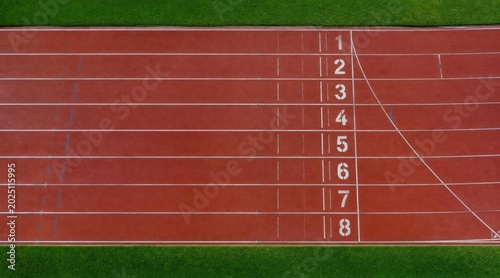 Overhead view of an empty red athletic running track with numbered lanes from 1 to 8 and surrounding green grass, ready for competition or training