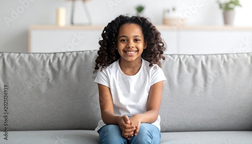 Smiling Young Girl Sitting on Gray Sofa in Bright Living Room