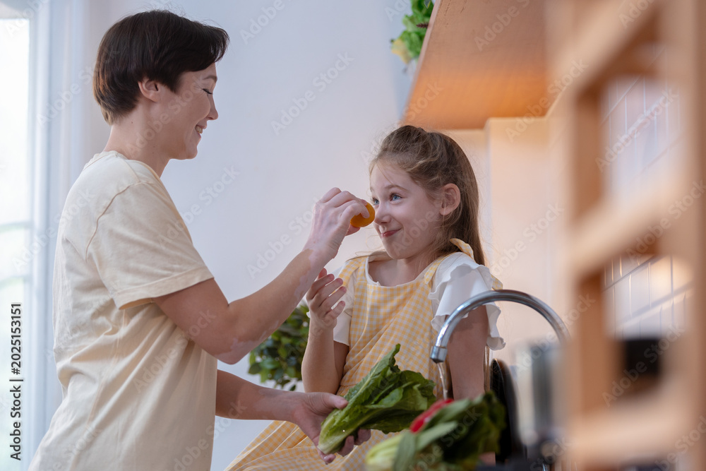 Obraz premium Happy mother and playful daughter cooking healthy food in bright kitchen showing joyful togetherness and loving family lifestyle during morning meal preparation with fresh vegetable