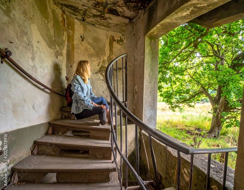 Thoughtful Young Woman Sitting on Worn Spiral Staircase in Abandoned Building Interior
