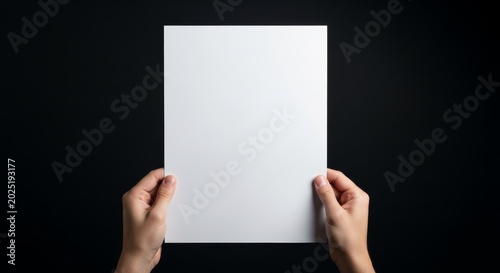 Man holding empty white sheet of paper. Blank vertical document for office presentation or communication message. Clean cardboard template mockup against dark background for design.