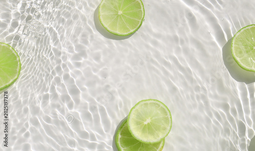 Fotografija Fresh green lime slices floating in clear water with ripples texture