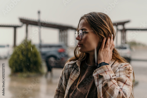 Woman rain autumn young female with glasses and plaid shirt standing outdoors in city park during rainy day