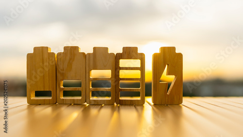 Battery wooden blocks showing charge level with lightning bolt icon at sunset for renewable energy, sustainability infrastructure, technology power and carbon neutral business concept.
