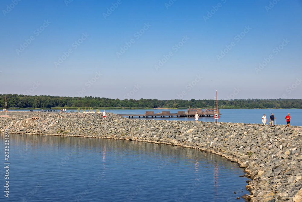 Fototapeta premium People walking on a stone pier in the sunshine