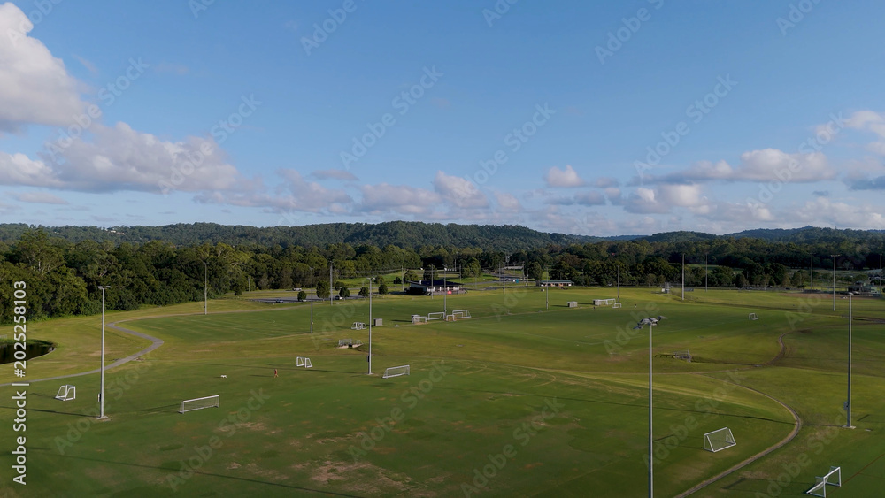 Obraz premium Wide Aerial View of Green Soccer Fields and Forested Hills Under Blue Sky