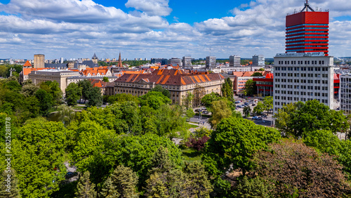 Schilderij op canvas Aerial drone view of the Poznan city skyline featuring the red Collegium Altum skyscraper and neighboring modernist high-rise building, surrounded by green park trees and historic urban architecture