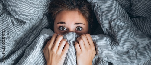 A terrified woman in bed with a blanket over her face is seen from above.