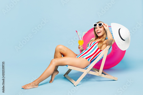 Full body young beautiful fun sexy woman wear bikini swimsuit lower glasses rest near hotel pool lies on deckchair drink cocktail isolated on plain blue background Summer vacation sea sun tan concept