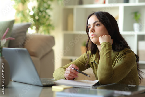 Fotografie Distracted young student looking away wasting time at home