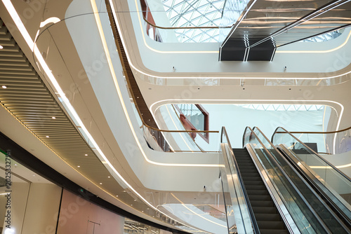 Obraz na plátne Wide angle view of modern shopping mall interior featuring escalators, curved architecture, glass roof, and retail circulation design
