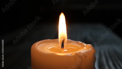 Close-up of a lit candle with a flickering flame in the darkness.