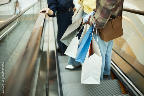 Fotografía Close up of young adult women carrying shopping bags while riding escalator in mall, representing retail spending and consumer behavior
