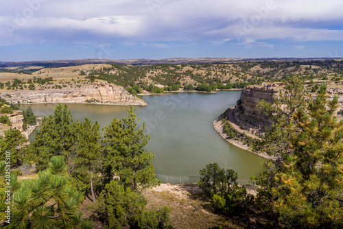 Fotografie Reservoir framed by sandstone bluffs and pine hills in Guernsey State Park, Wyoming, highlighting quiet Great Plains canyon terrain