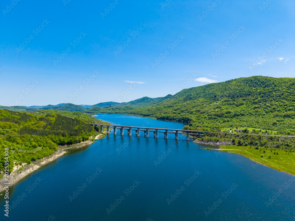 Obraz premium Clear blue water flows under the bridge surrounded by green hills and blue sky in a scenic view of nature and landscape in the daytime