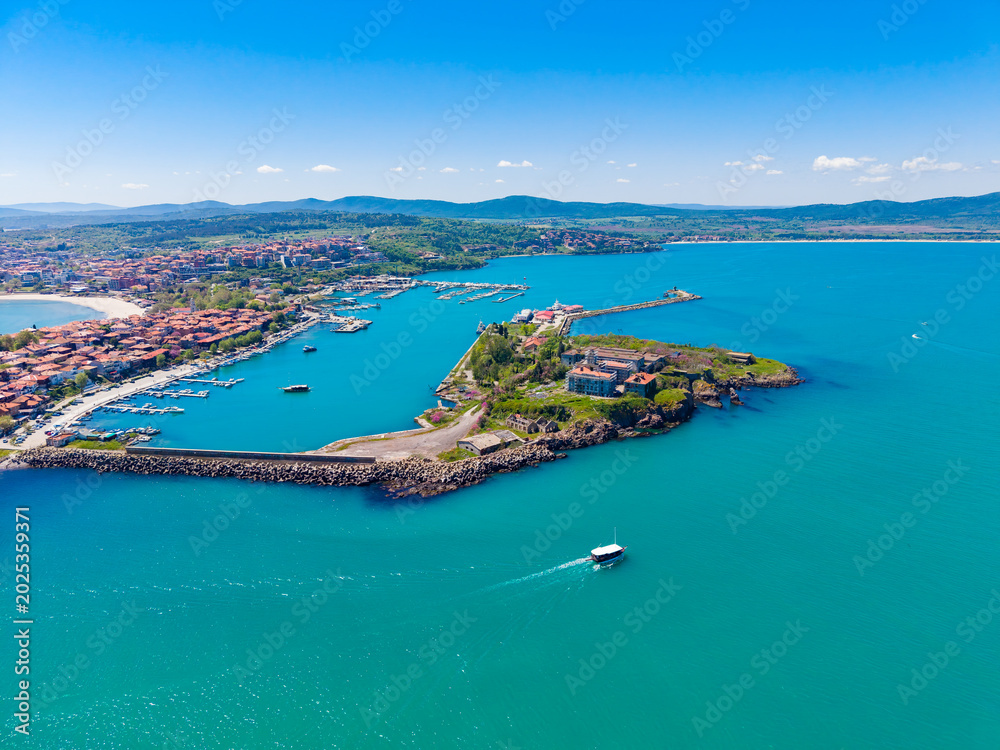 Fototapeta premium Bright day over a coastal town with a marina, boats, and green land by the water, showing a clear blue sky and hills in the background