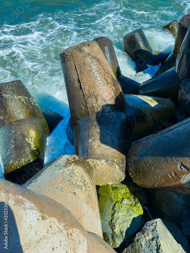 View of large concrete blocks along the shoreline with waves crashing at midday in a coastal location