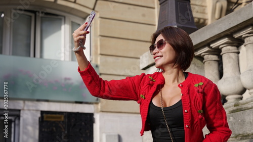 Canvastavla A cheerful Asian woman in a red cropped cardigan and sunglasses smiles while hol
