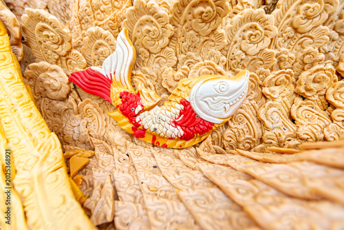 Fotografi Exquisite Thai wax sculpture detail featuring a brightly colored red and white fish amidst carved patterns