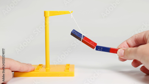 Cuadro en lienzo Hands Demonstrating Magnetic Attraction Using Bar Magnets on a Yellow Stand