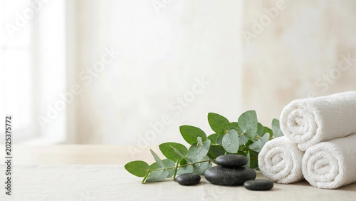 Towels arranged with smooth black stones and fresh green eucalyptus leaves create a serene atmosphere on a wooden spa table for a relaxing wellness experience that promotes total inner peace.