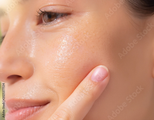Close-up of young woman touching oily skin on cheek with finger examining pores