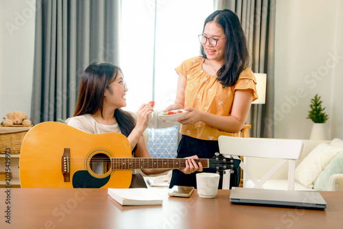 Valokuva Two Asian girls enjoyed themselves at home, singing and playing classical guitar, while another friend kindly offered them strawberries and chatted like typical teenagers